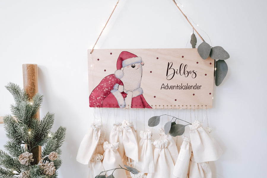 Adventskalender aus Holz, Holzschild bedruckt mit Eisbär im Weihnachtsmannkostüm und Namen, darunter Stoffsäckchen