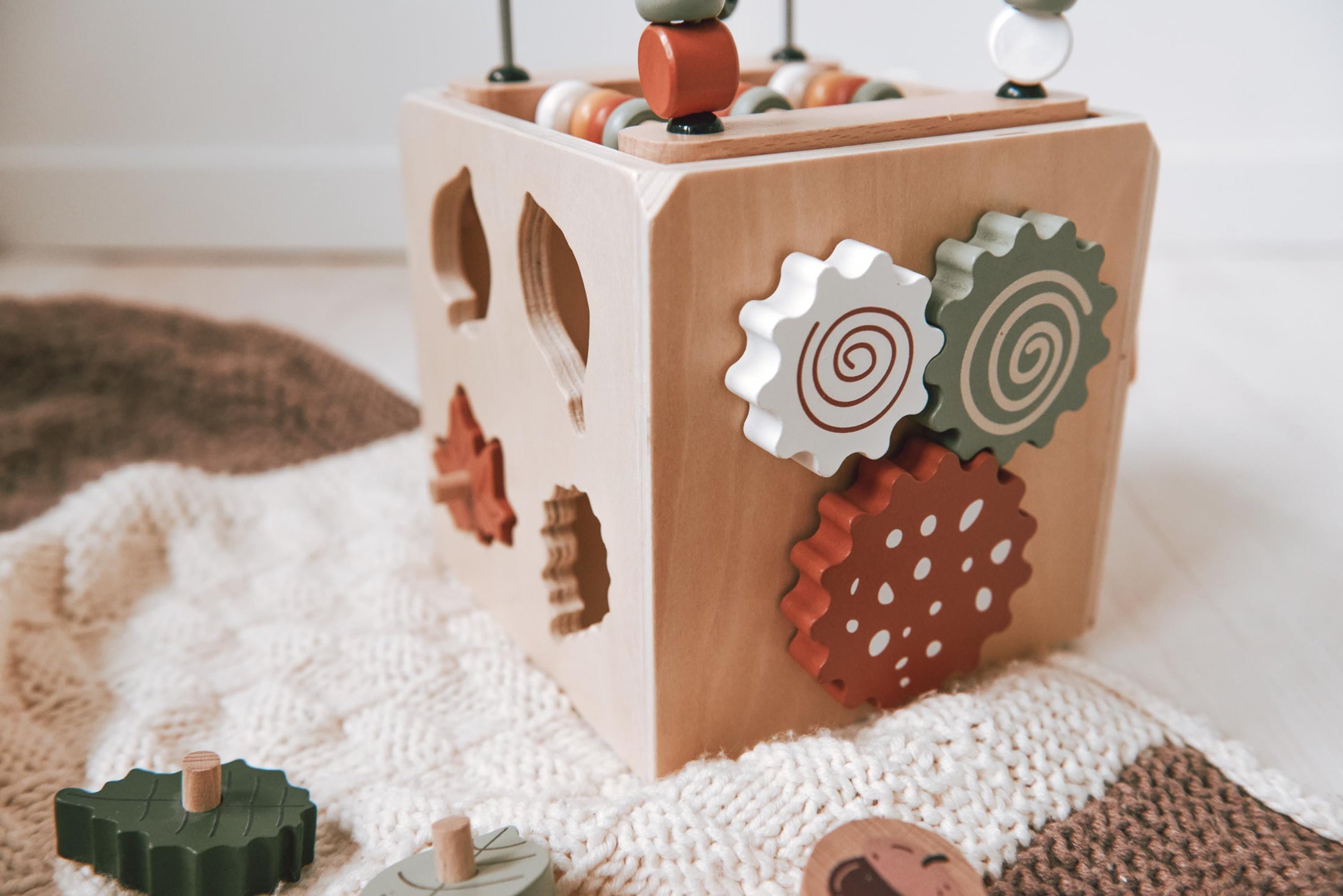 Spielwürfel aus Holz gesättigten warmen Farben, zeigt Schiebespiele, Steckspiel und Zahnrad auf der Oberfläche